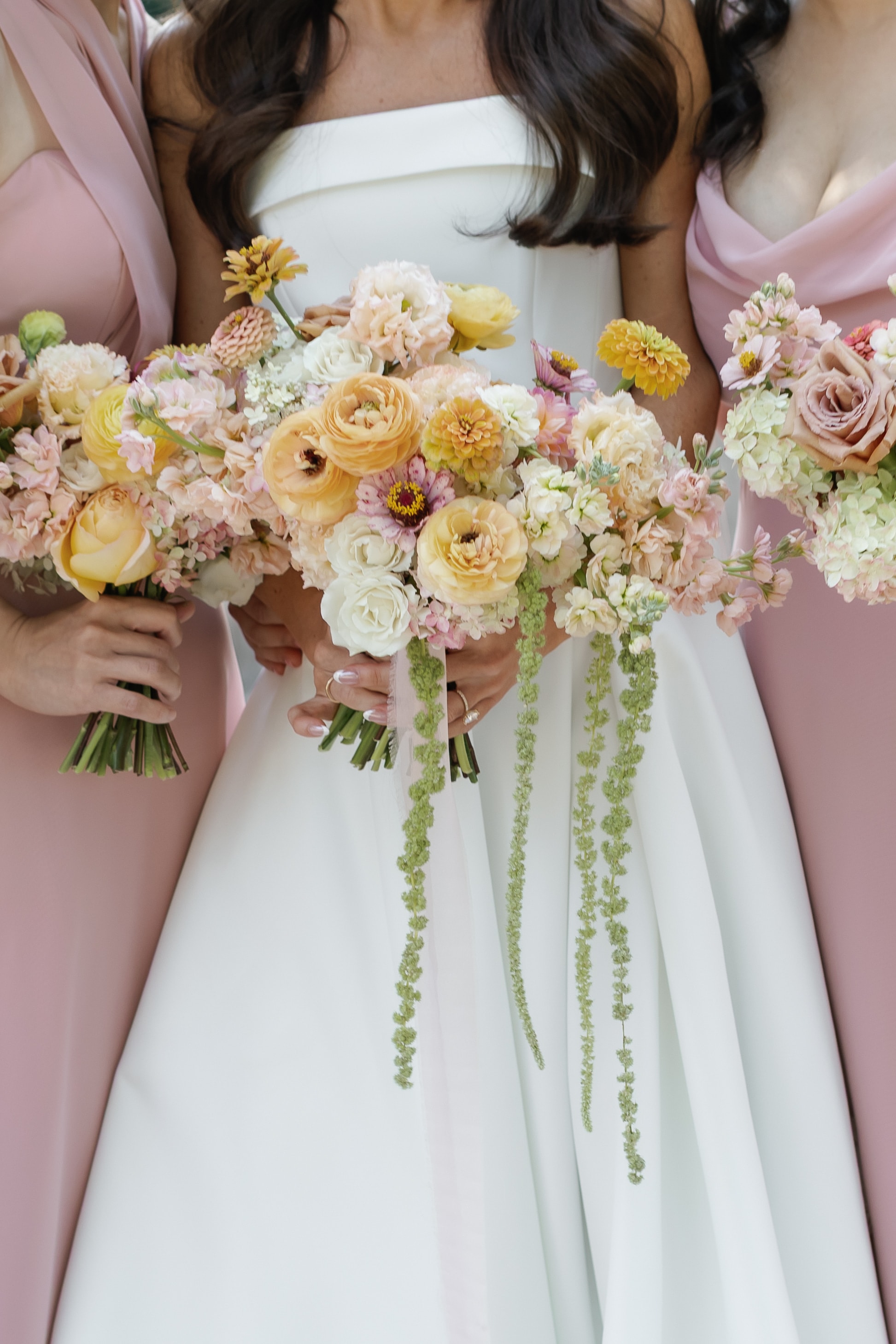Bride and bridesmaids in pink dresses holding lush peach and cream bouquets with trailing amaranthus