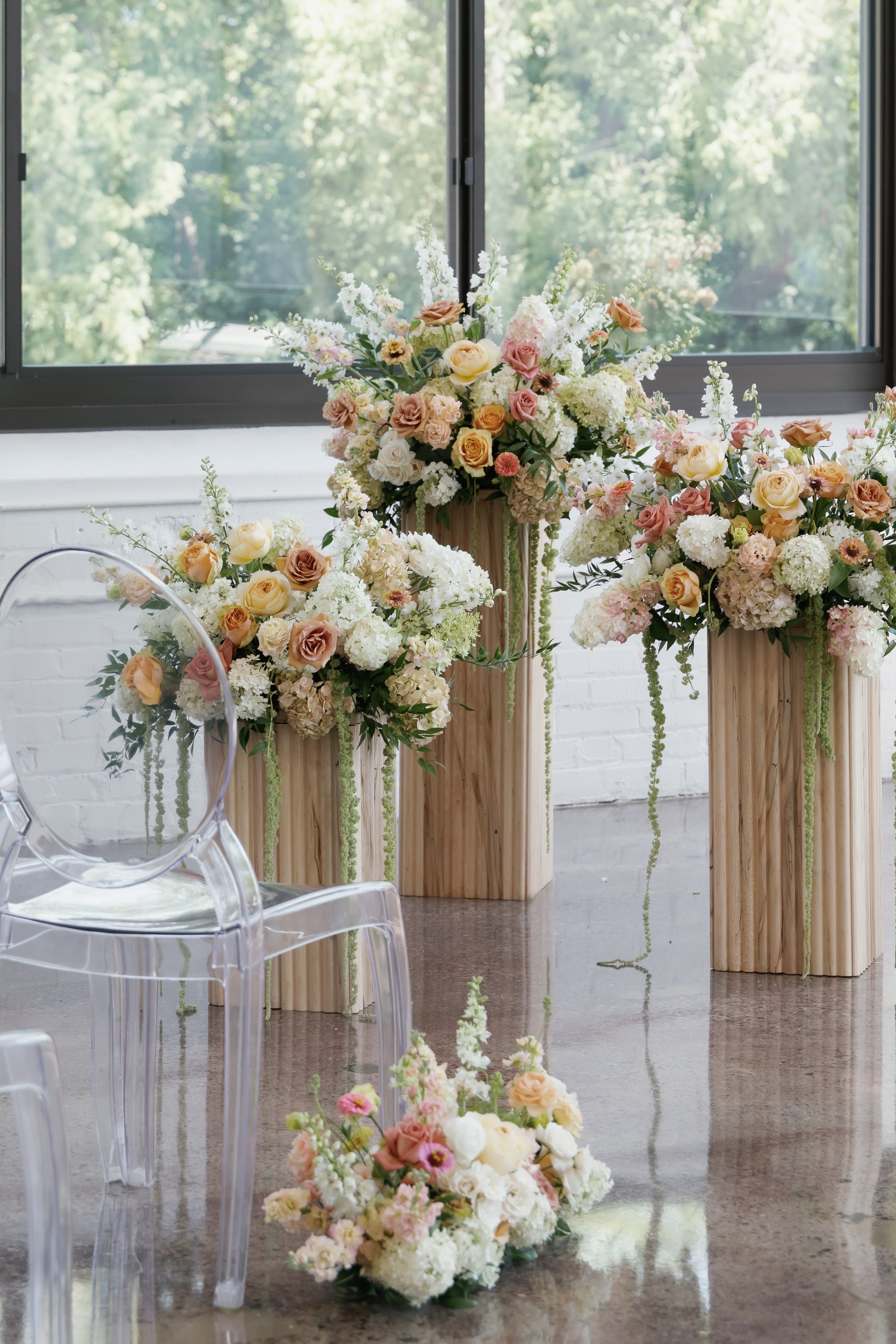 Peach and cream floral arrangements on wood pedestals with ghost chairs at Urban Daisy ceremony