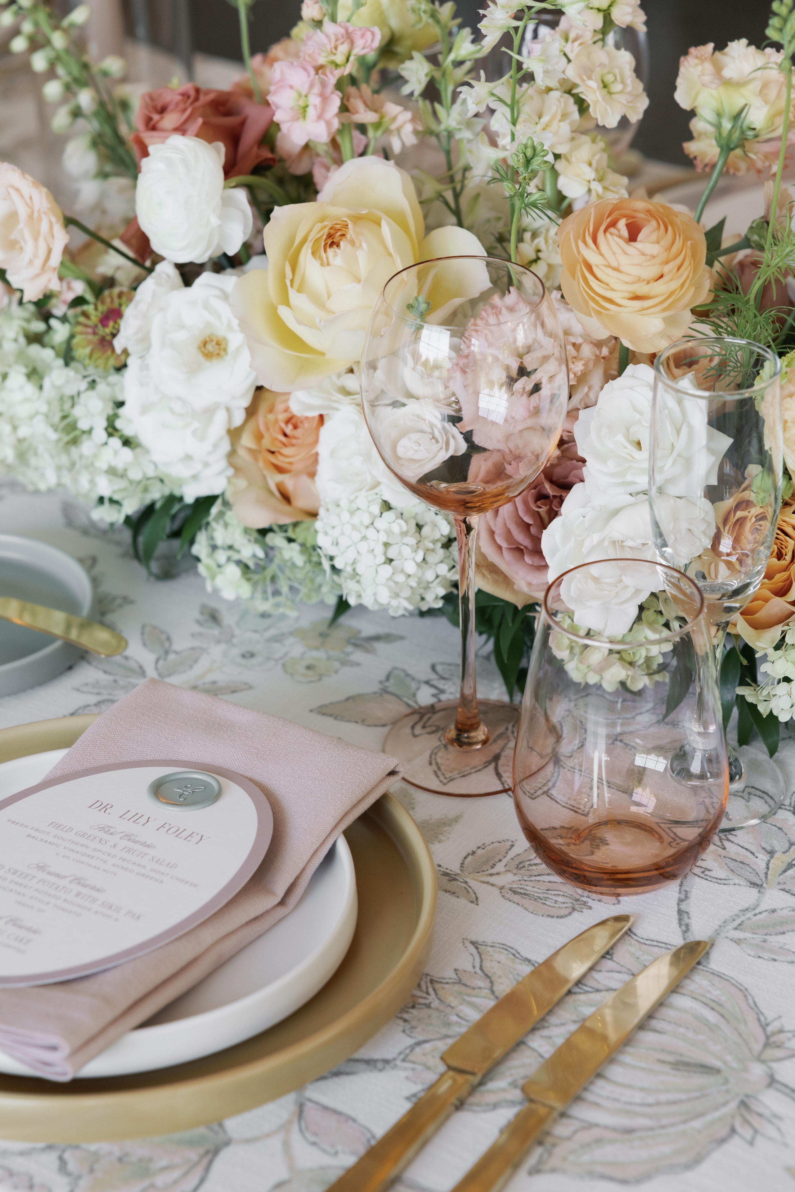 Close-up of wedding place setting with wax seal menu card pink glassware and floral centerpiece