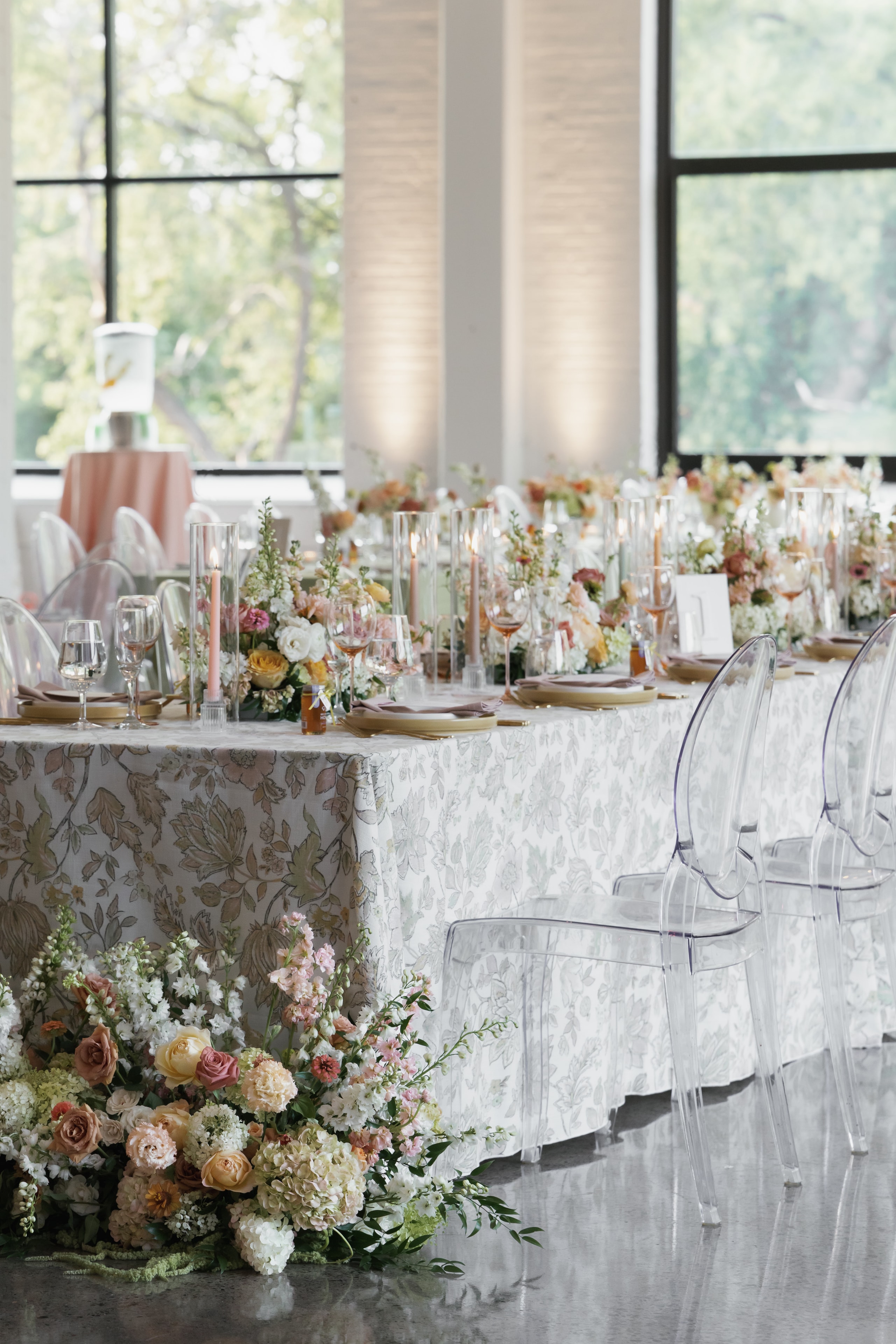 Elegant wedding reception head table with peach and blush floral runner and ghost chairs
