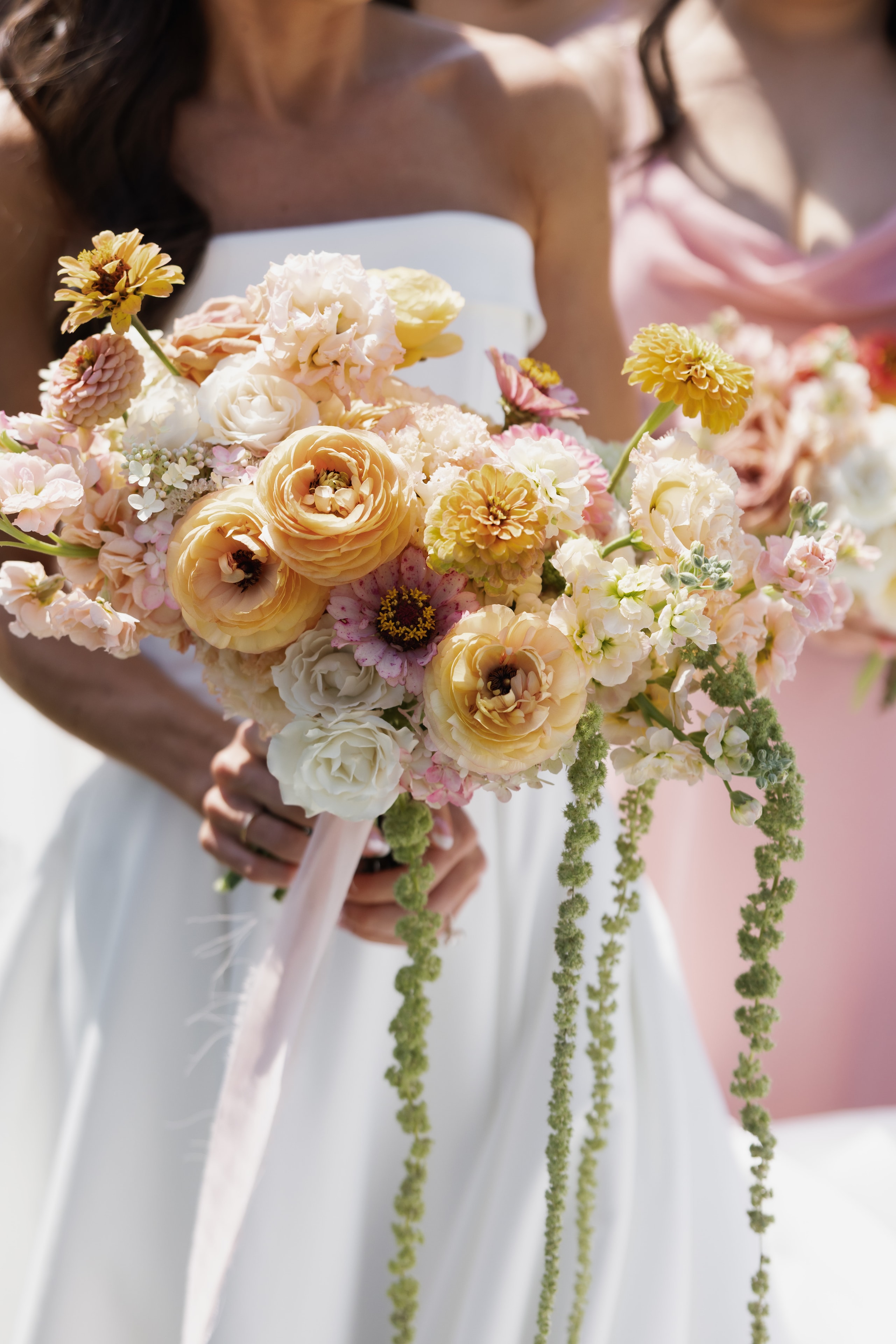 Bride holding lush bouquet of peach ranunculus yellow zinnias and trailing amaranthus
