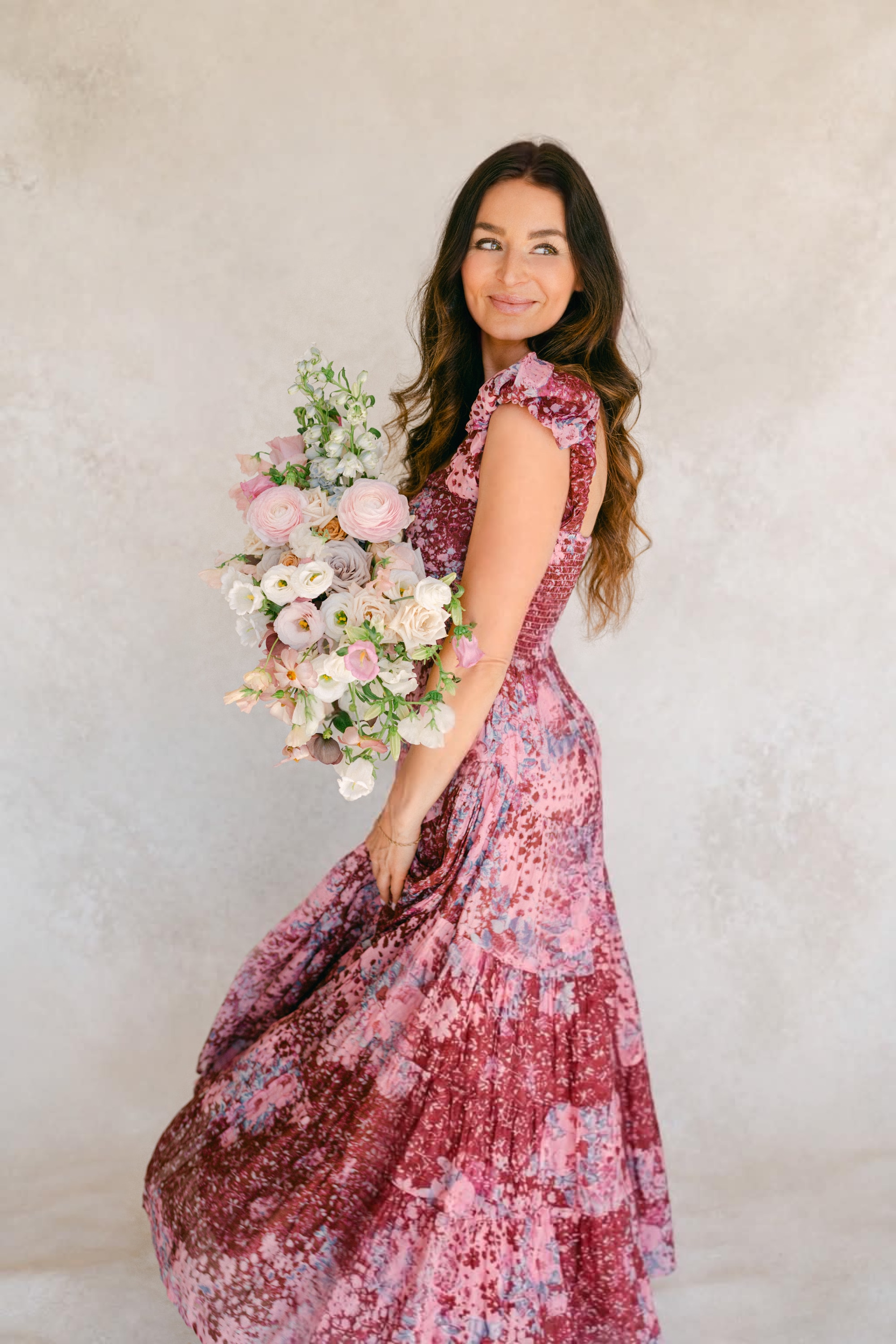 Woman in floral dress smiling over shoulder holding lush pastel bouquet