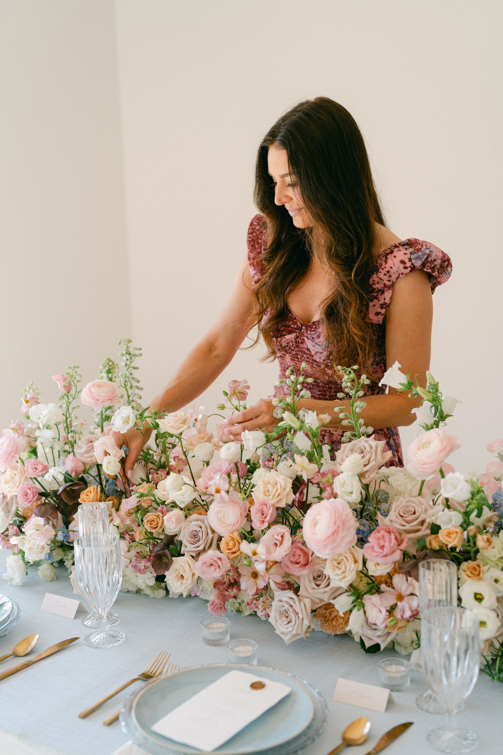 Woman in burgundy dress arranging floral centerpiece at table
